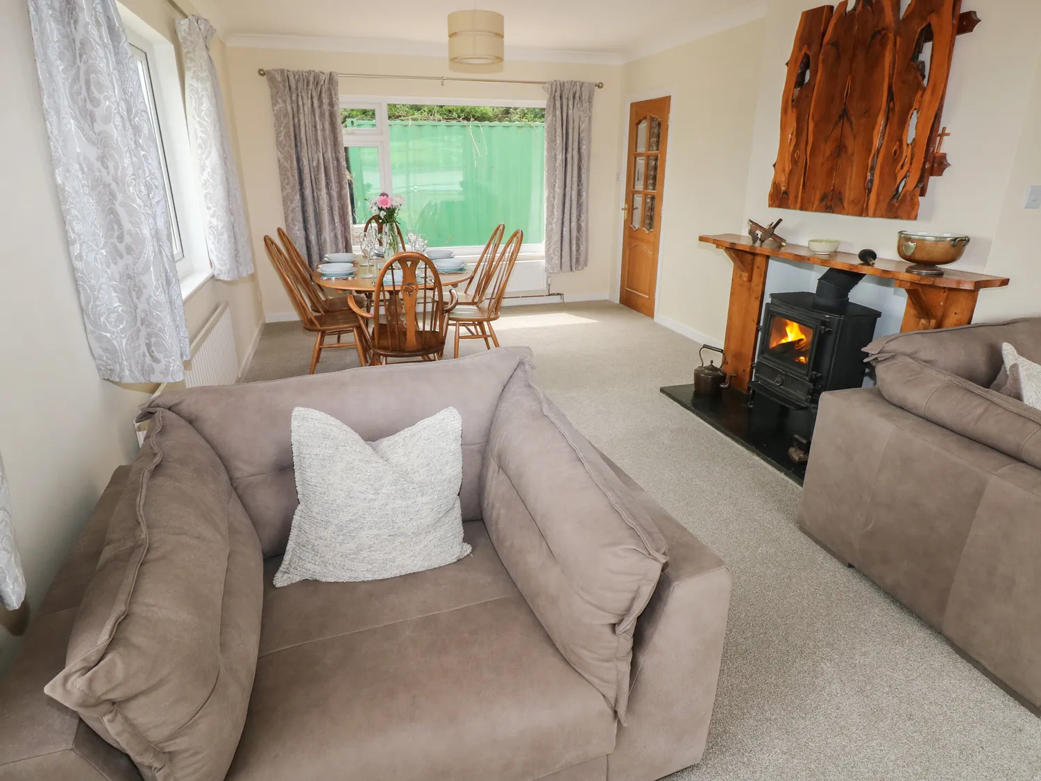 A view behind a large chair showing a dining table and wood burner. There are also two large windows.