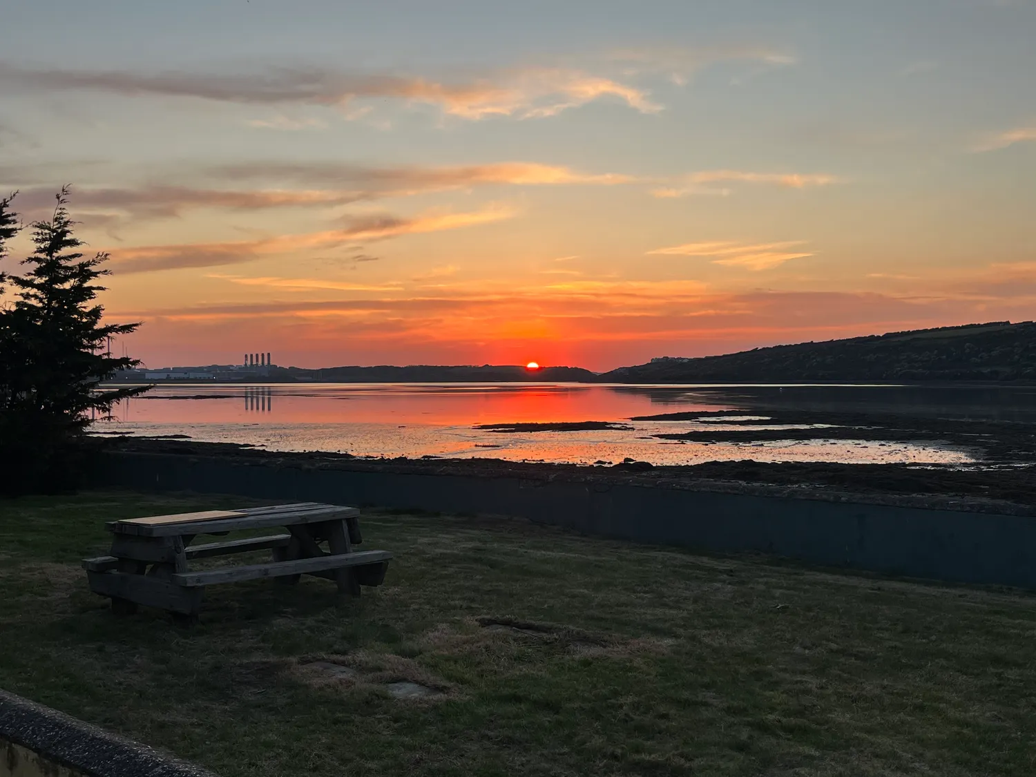 The garden showing the picnic bench looking over the river while the sun sets in the distance.