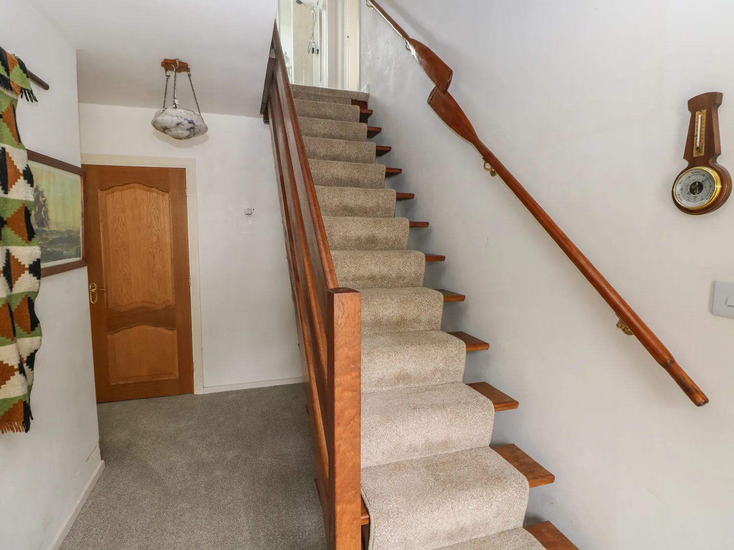 A carpeted hallway with wooden stairs going up the the first floor.